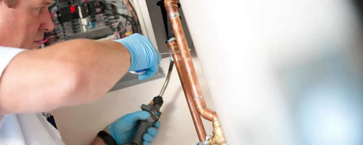 Water heater repair technician testing copper pipe connections and controls in Mansfield, MA